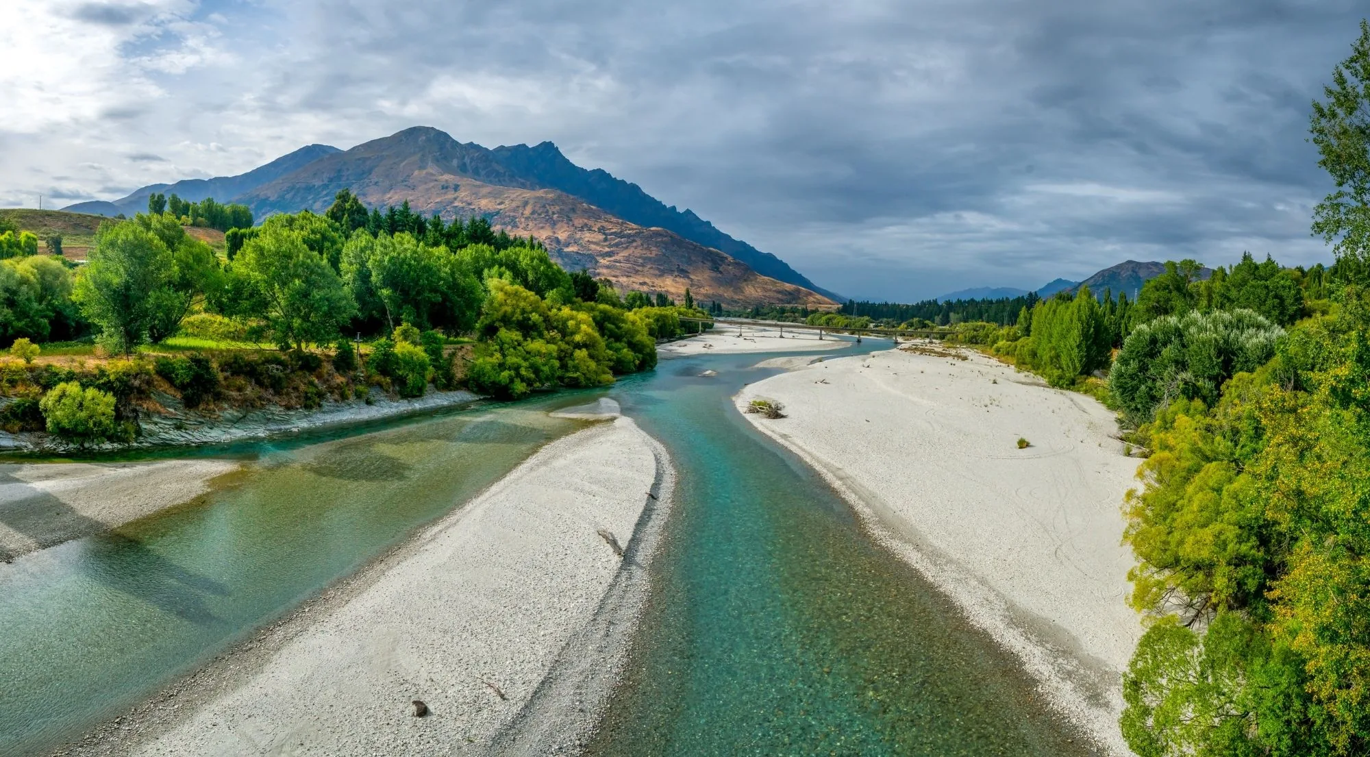 A wide river bend and shingle bar under a heavy, broken sky