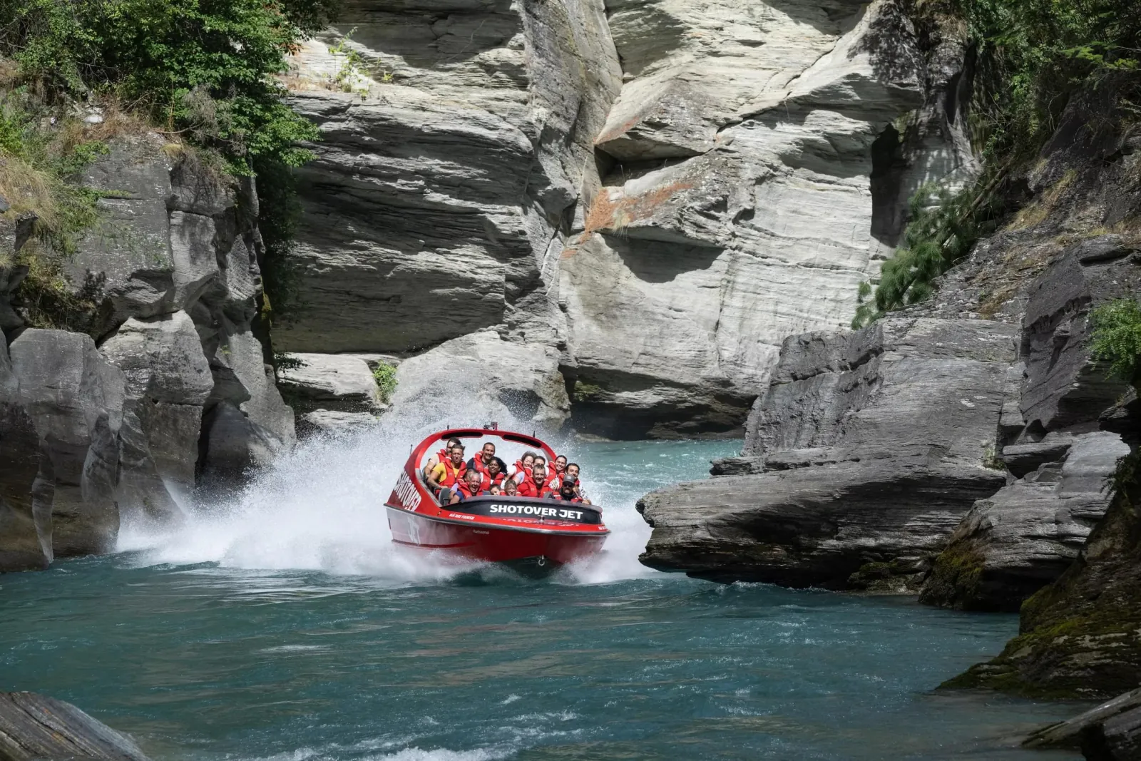 A red jet boat running a shallow reach between grey schist canyon walls