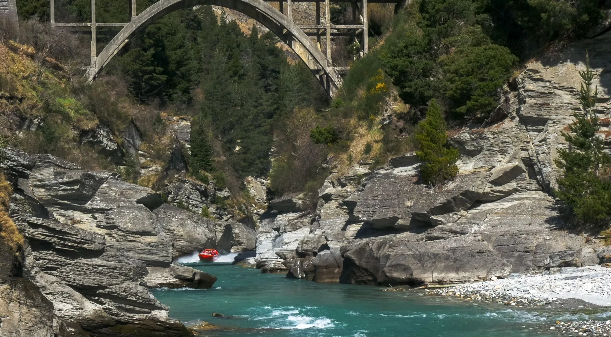 A red jet boat dwarfed by the grey schist walls of the Shotover canyon