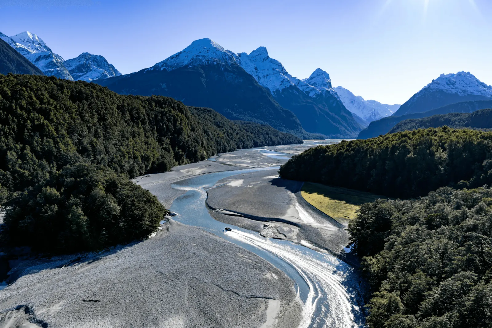A braided river winding through forest towards jagged mountains
