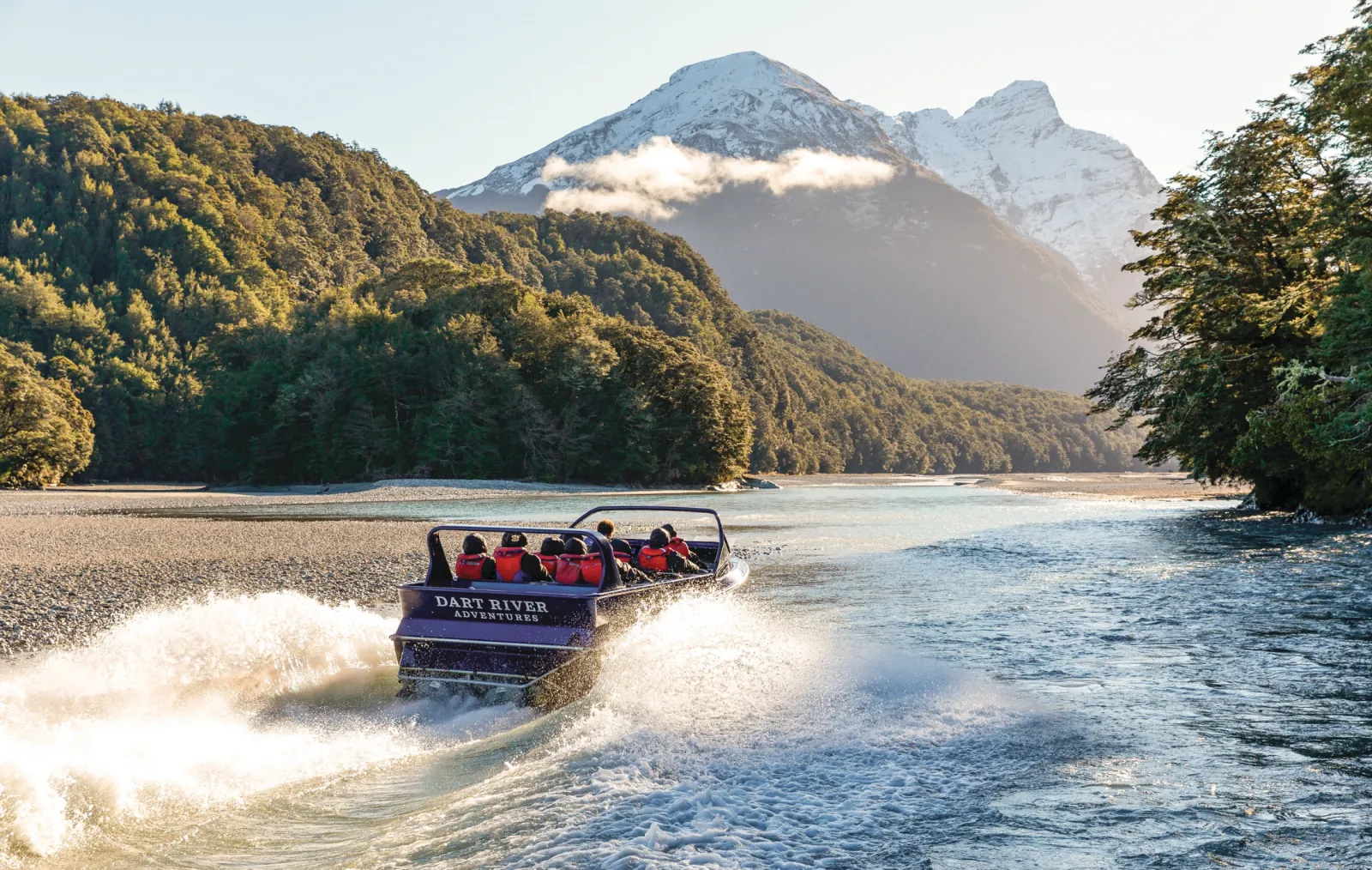 A jet boat throwing spray on a shingle-lined channel below a glacier valley