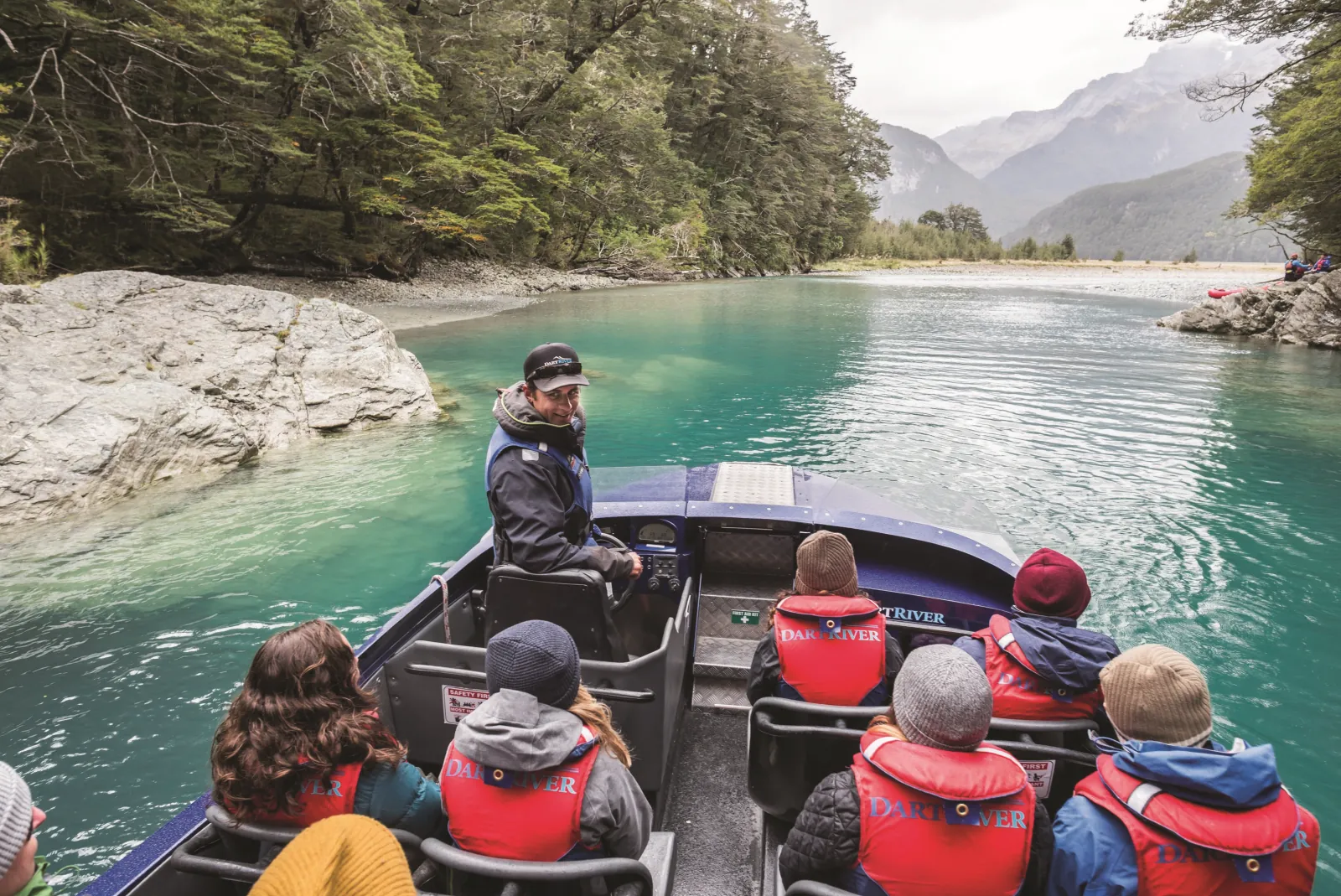 Passengers in red jackets aboard the boat with the driver-guide at the wheel