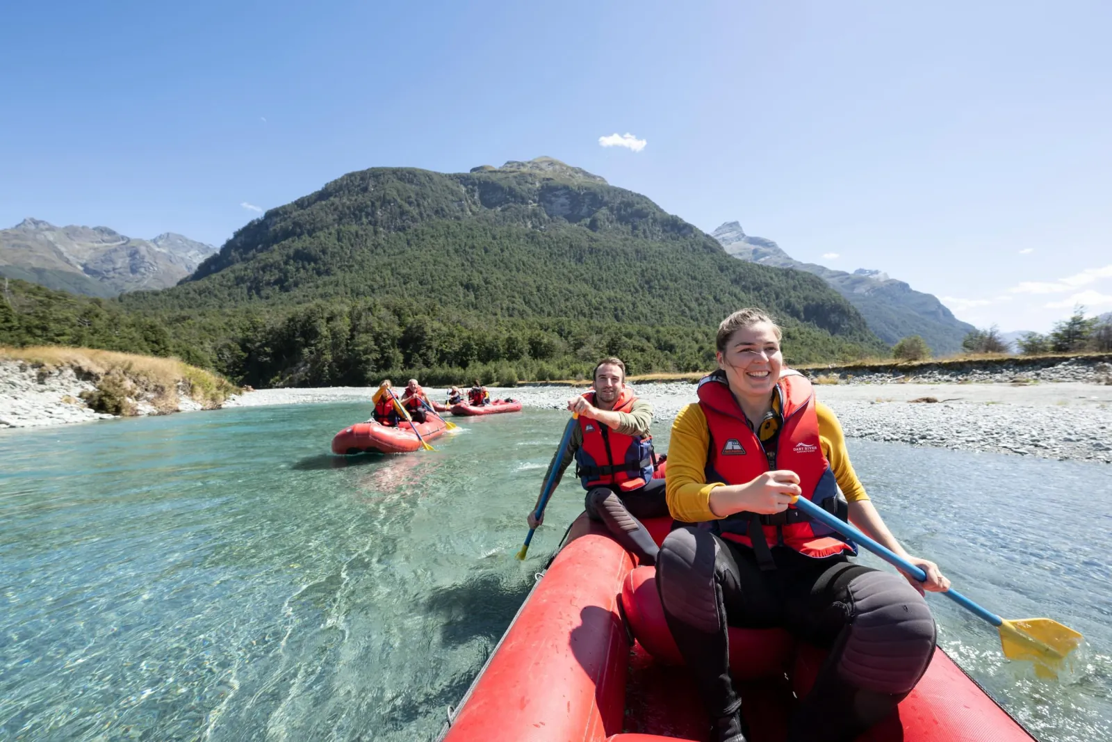 Two paddlers in a red Funyak canoe on a braided reach below the mountains