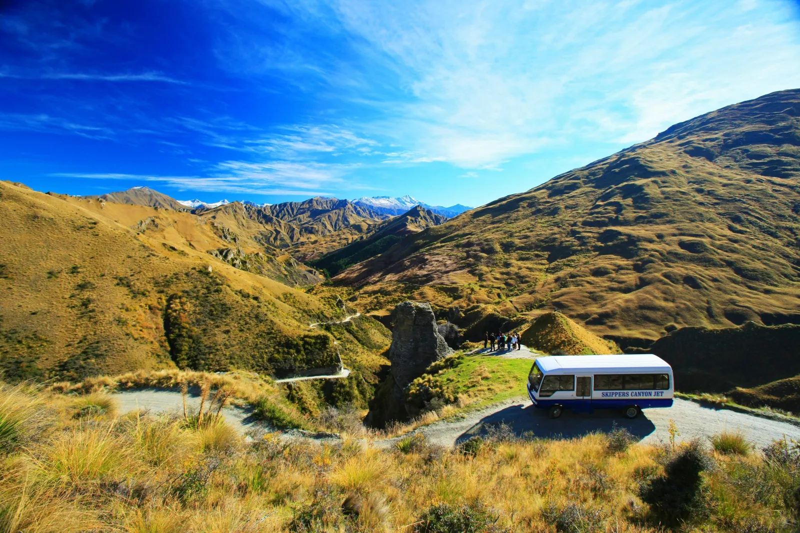 The Skippers Road cut into a steep tussock hillside, with a small bus on it