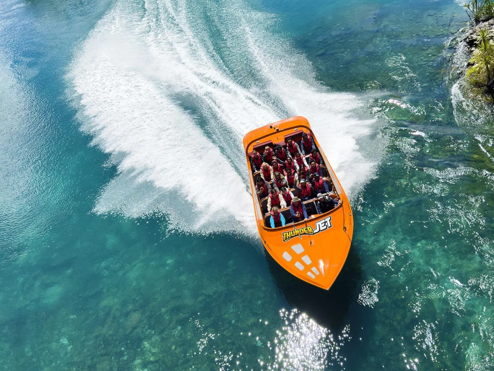 An orange Thunder Jet boat carving a turn on clear green water, seen from above