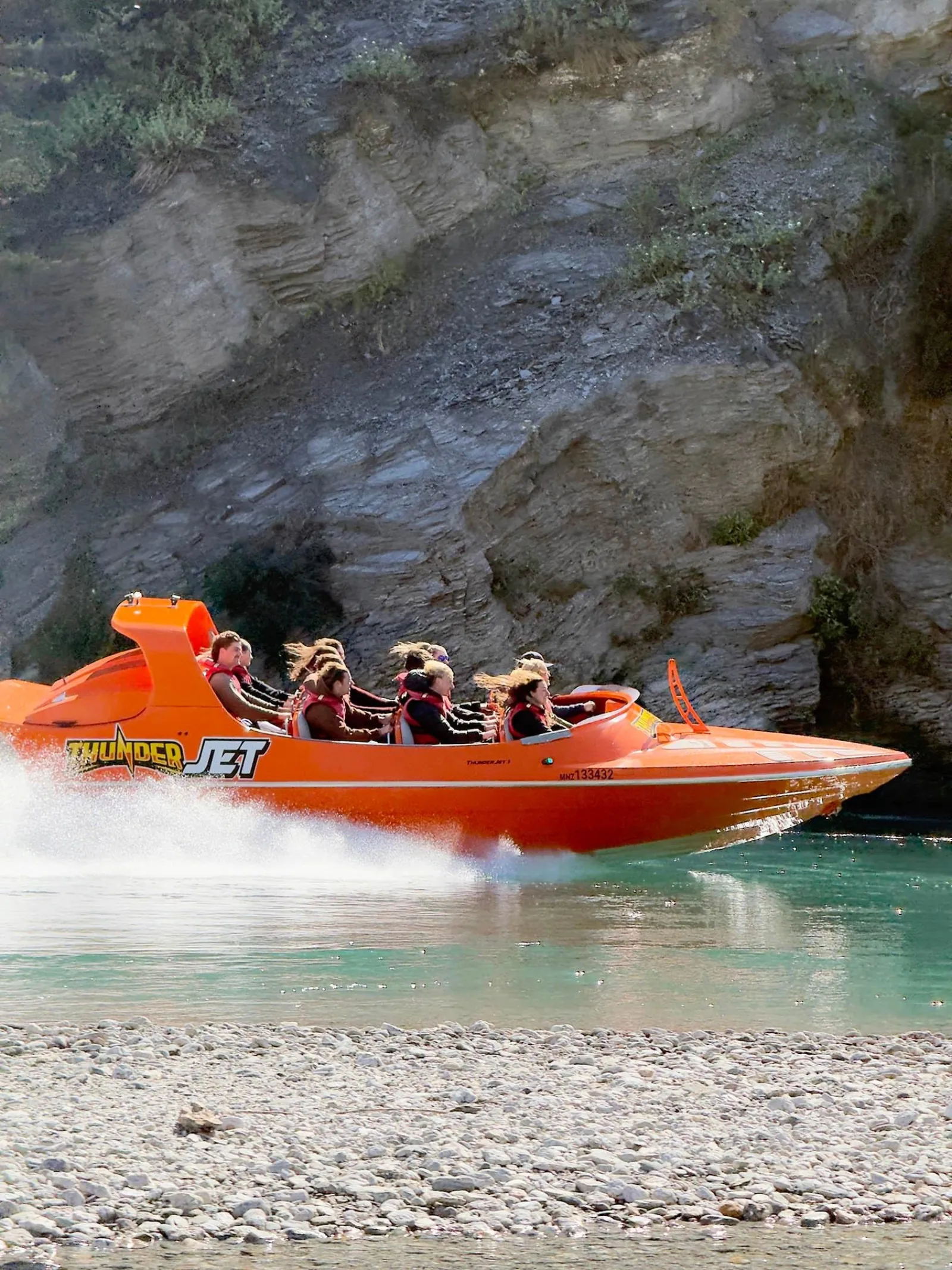 An orange Thunder Jet boat at speed against a dark rock face