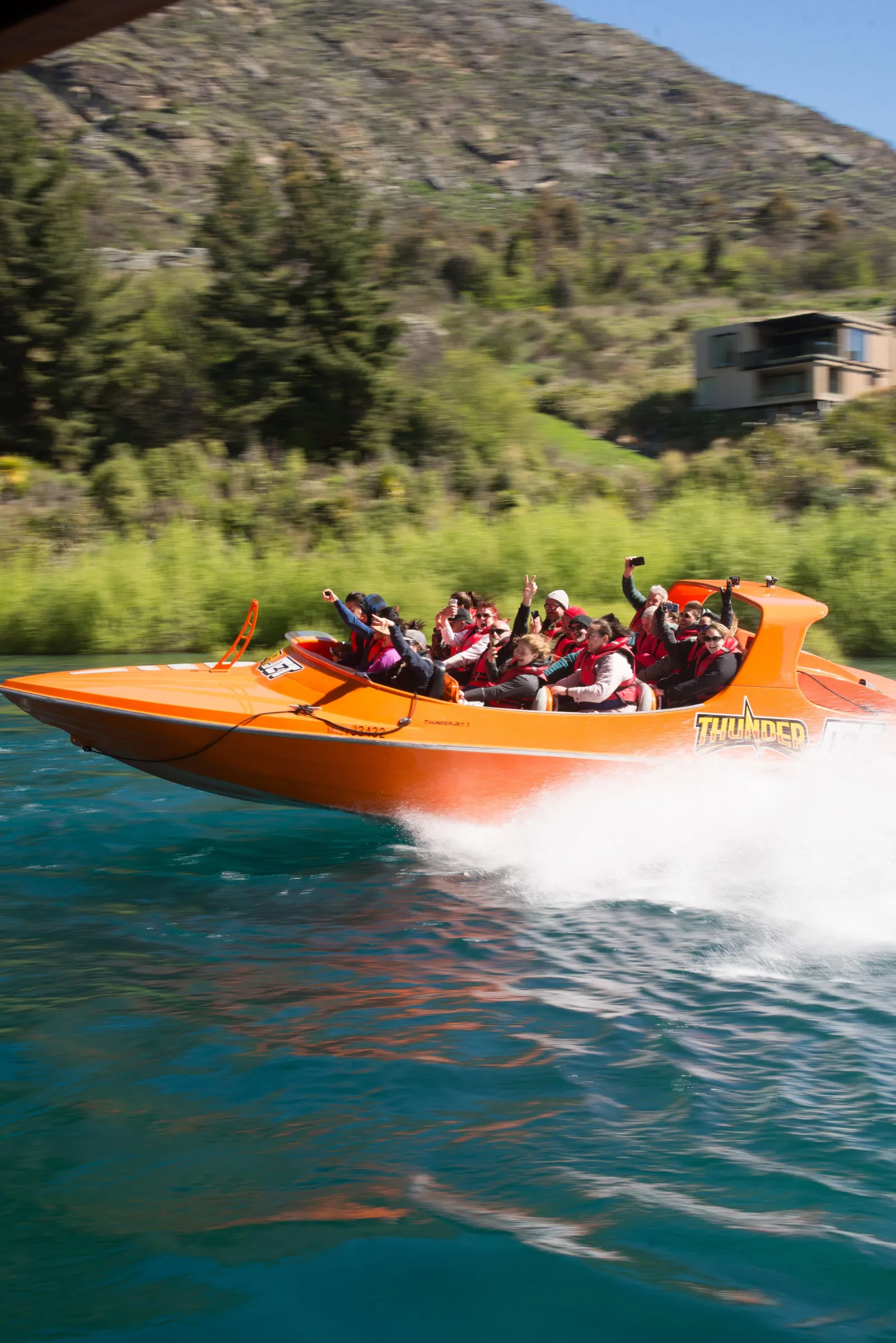 An orange jet boat blurring past a green riverbank at full speed