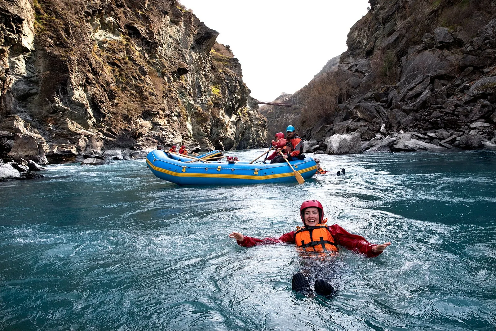 A swimmer floating beside a raft in calm green water between rapids