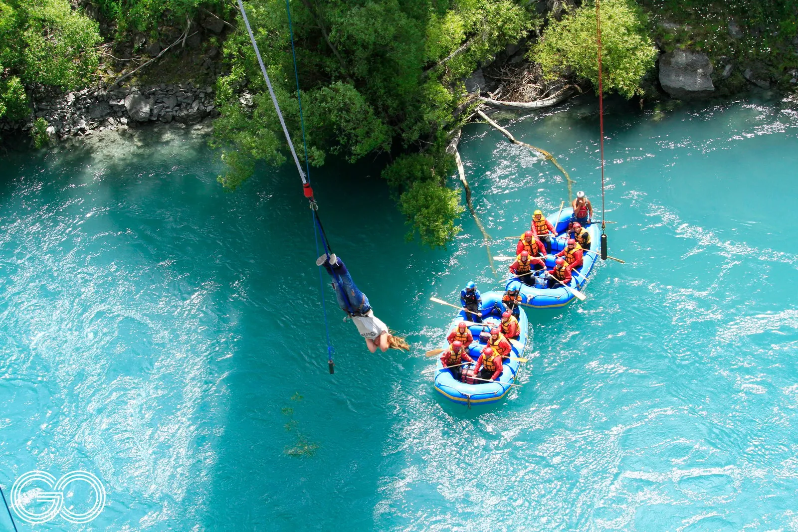 Aerial view of a raft on bright turquoise water with a guide on the bank