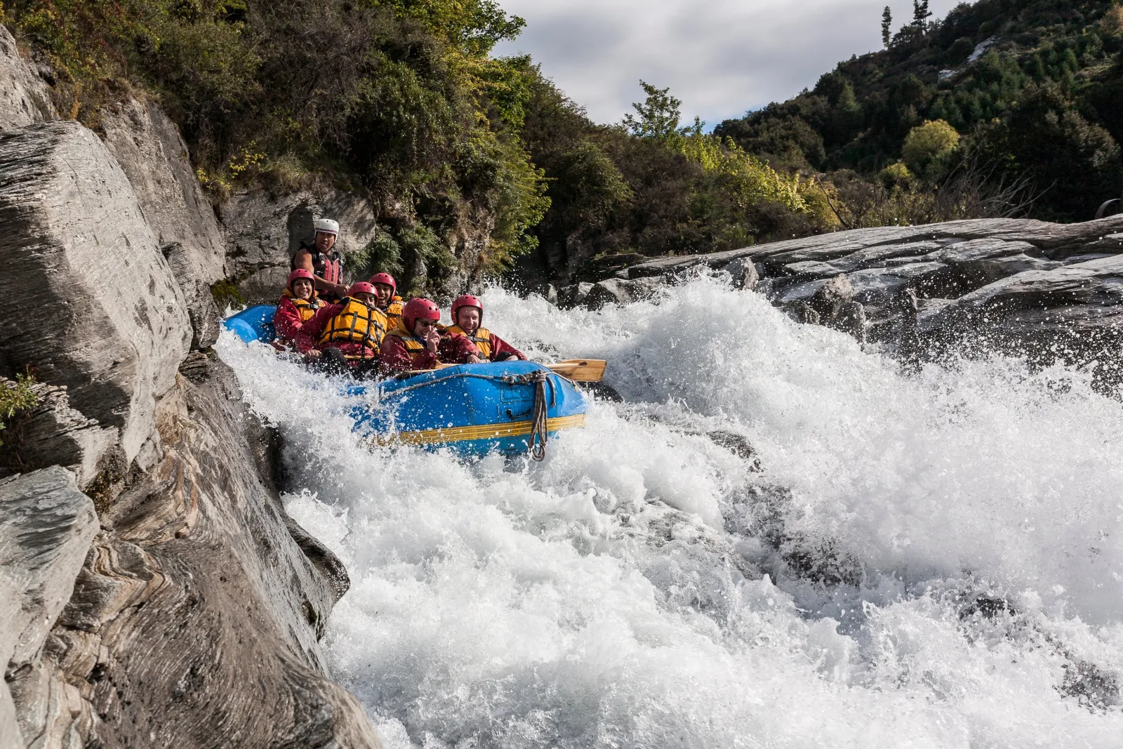 A raft dropping into a rapid below steep bush-covered banks