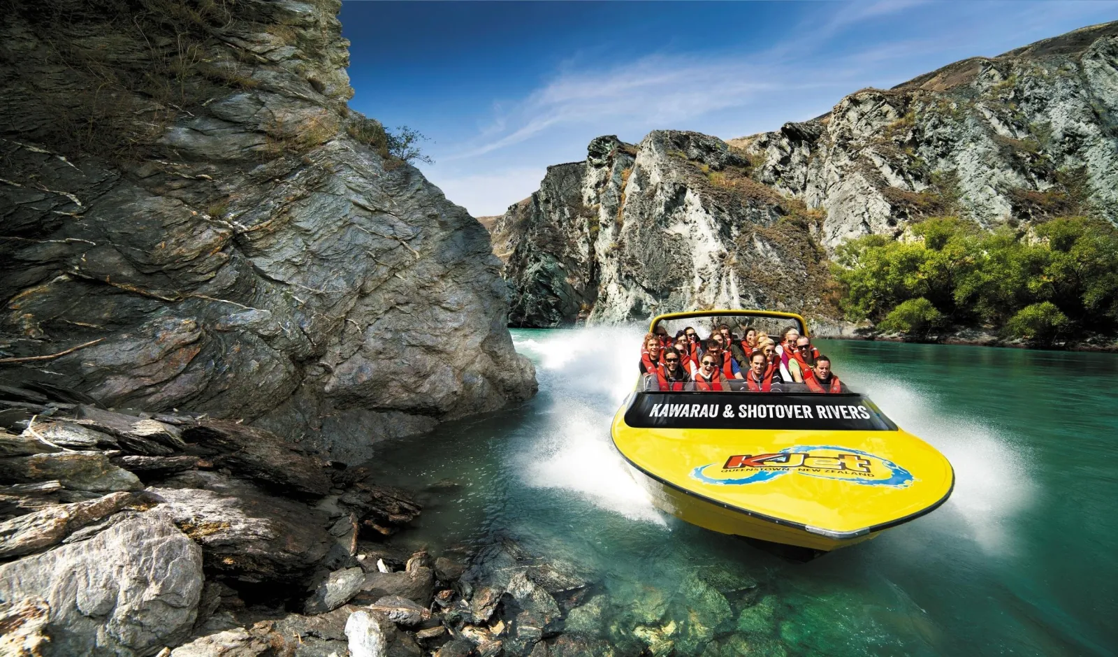 A yellow KJet boat turning below a steep rock bluff on the river