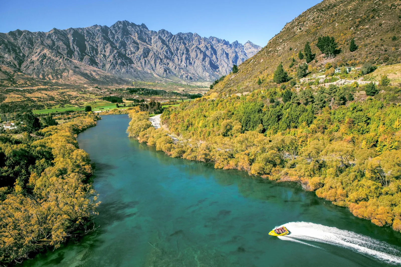 Aerial view of a jet boat on a green-blue river below the Remarkables