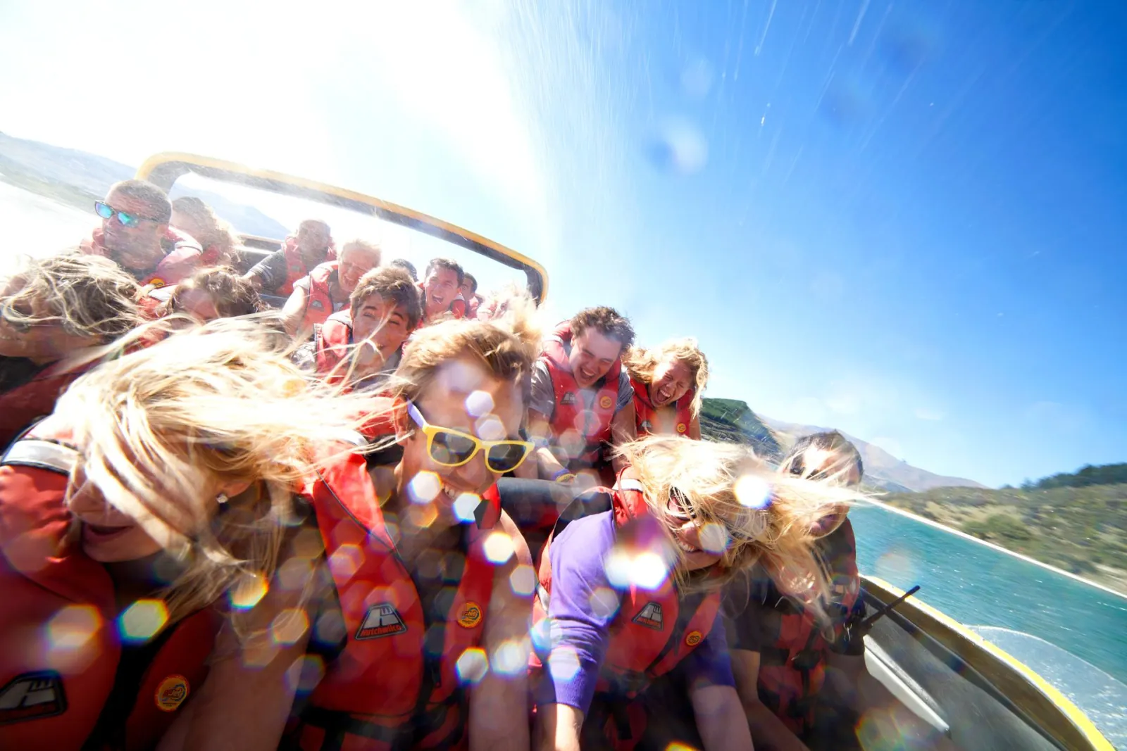Passengers in red life jackets packed into the boat during a spin, water flying