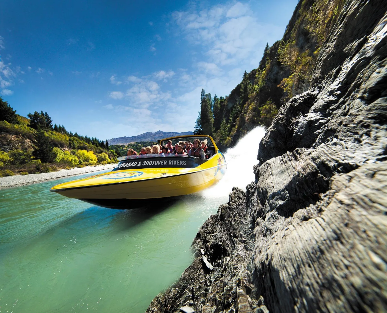 A yellow KJet boat heeled over against a dark rock wall at speed
