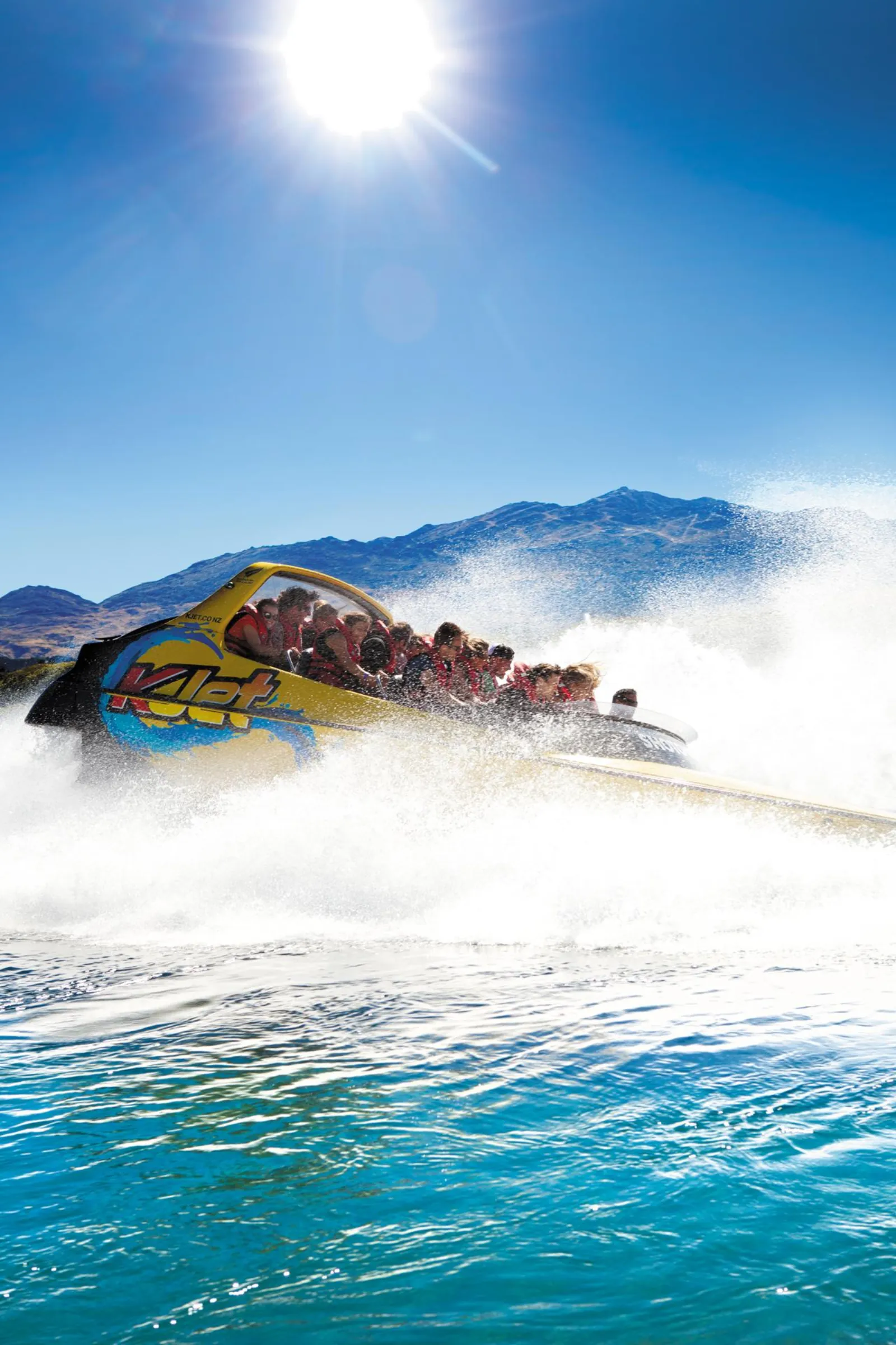A yellow KJet boat in a full spin under bright sun, water sheeting off the hull